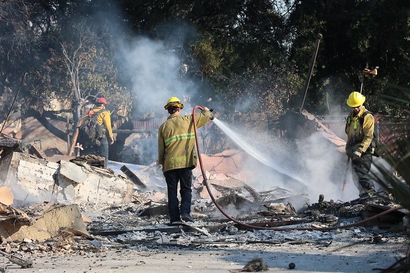 A crew hoses down the smoldering remains of a building in Altadena.