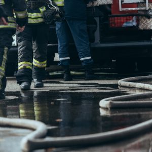 Firefighters in protective gear standing near a fire truck with water hoses on a wet pavement.